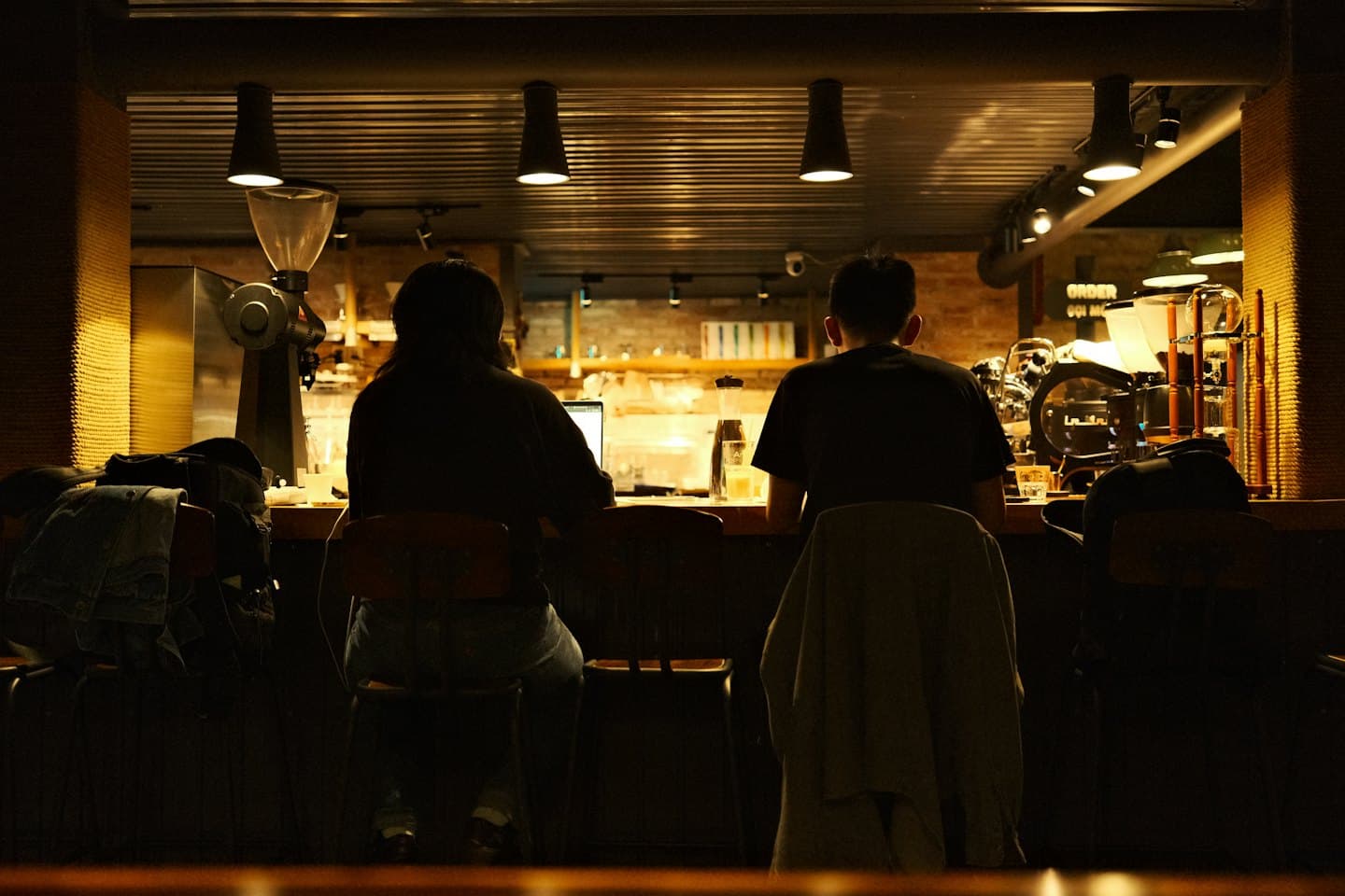 Due persone siedono al bancone di un bar usando un laptop.