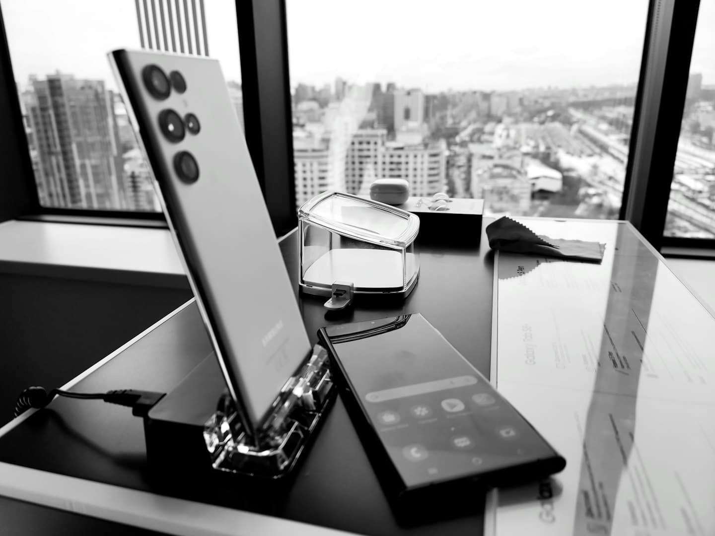 Due smartphone e accessori su una scrivania con vista sui binari della città.